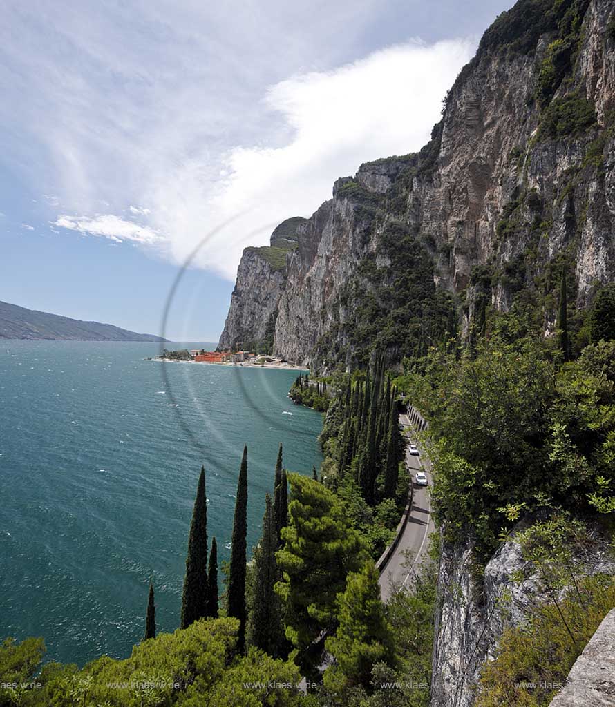 Tremosine, Blick ueber Gardaseestrasse mit Autos in mediteraner vegetation, Zypresssen mit Gadasee und schroffen Felswaenden, im Hintergind Campione del Garda; Tremosine, view over lake garda street with cars, cypress trees ,lake Garda, rocks and the village Campione del garda