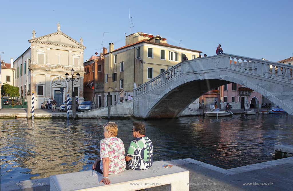 Chioggia Kanal Vena Canale Vena zwei Frauen Italinerinnen auf Steinbank sitzend vor der Vena Bruecke in stimmmungsvollem Licht; Canal Vena two women sitting ona stone bank in front ofh Vena bridge Ponte Vena in evening light