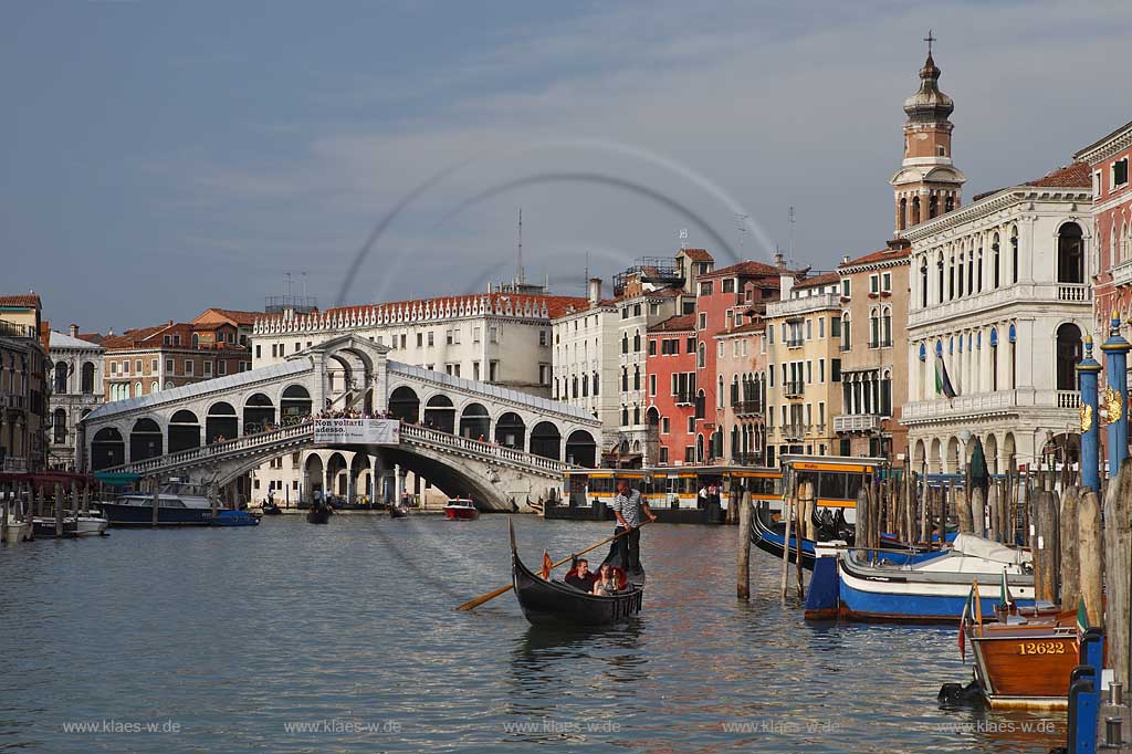 Venedig, Rialto, Blick von Riva del Carbon auf Kanal Grande mit der Rialtobruecke Ponte di Rialto, Kirchturm Campanile der Kirche Chiesea dei San Bartolomeoi, Gondel mit Gondoliere mit T Shirt quergestreift und junges Paar in Gondel sitzend; Venice Rialto view from Riva del Carbon to Canal Grande with Rialto bridge, gondola and gondolier in raye transversalement t-shirt, joung couple sitting in gondola, tower of church of San Bartolomeo