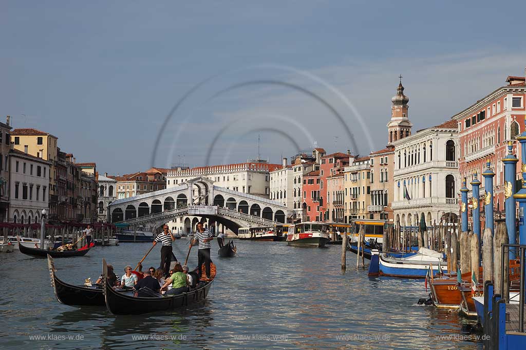 Venedig, Rialto, Blick von Riva del Carbon auf Kanal Grande mit der Rialtobruecke Ponte di Rialto, Kirchturm Campanile der Kirche Chiesea dei V, mehrere Gondeln mit Gondoliere mit T Shirt quergestreift und Personen, Familien in mittlerem Alter in Gondel sitzend, zwei Gondeln Vordergund betont im Bild; Venice Rialto view from Riva del Carbon to Canal Grande with Rialto bridge, several gondola and gondoliers in raye transversalement t-shirt, midlife people middle age person sitting in gondola, tower of church San Bartolomeo
