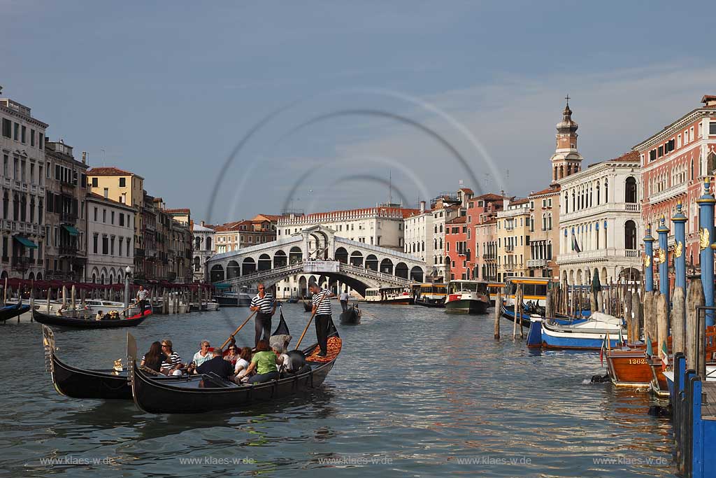 Venedig, Rialto, Blick von Riva del Carbon auf Kanal Grande mit der Rialtobruecke Ponte di Rialto, Kirchturm Campanile der Kirche Chiesea dei V, mehrere Gondeln mit Gondoliere mit T Shirt quergestreift und Personen, Familien in mittlerem Alter in Gondel sitzend, zwei Gondeln Vordergund betont im Bild; Venice Rialto view from Riva del Carbon to Canal Grande with Rialto bridge, several gondola and gondoliers in raye transversalement t-shirt, midlife people middle age person sitting in gondola, tower of church San Bartolomeo