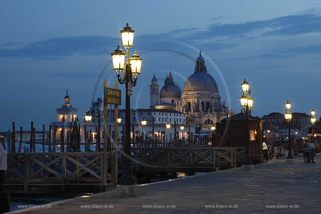 Venedig Blick von Riva degli Schiavoni ueber Mole mit Gondeln und Kanal di San Marco zur Basilika di Santa Maria della Salute zur Blauen Stunde mit Strassenlaternen beleuchtet, illuminiert; Venice view from Riva degli Schiavoni with mole, gondola and canal di San Marco to basilica San Maria della Salute in nightlight, evening light blue hour with illumination and glowing lantern