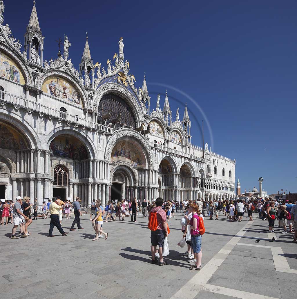 Venedig Markusplatz Blick auf die Hauptfassade mit Hauptportal der Markuskirche mit Menschen, Touristen, Dogenpalast, der Saeule mit der Skulptur des Markusloewen und Isola San Giorgio Maggiore; Venice Piazza San Marco with view to facade of Basilica di San Marco with the main portal and people, tourists on the square, Palazzo Ducale, column with sculpture of Lion of San Marco and the Isola San Giogio Maggiore in far background