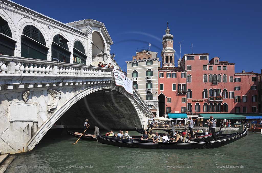 Venedig Bruecke Ponte di Rialto mit Kanal Grande seitlich fotografiert mit  mehreren darunter herfahrenden Gondeln mit Gondolierie und Fahrgaesten, Menschen auf Bruecke stehend und schauend, gegenueber Riva del Ferro mit dem Kirchturm Campanile der Kirche Chiesa di San Bartolomeo; Venice sideways view to bridge of Rialo with Canal Grande, several gondola with gondoliers and several peopl sitting inside of gondola in the background Riva del ferro with the tower of church of San Bartolomeo