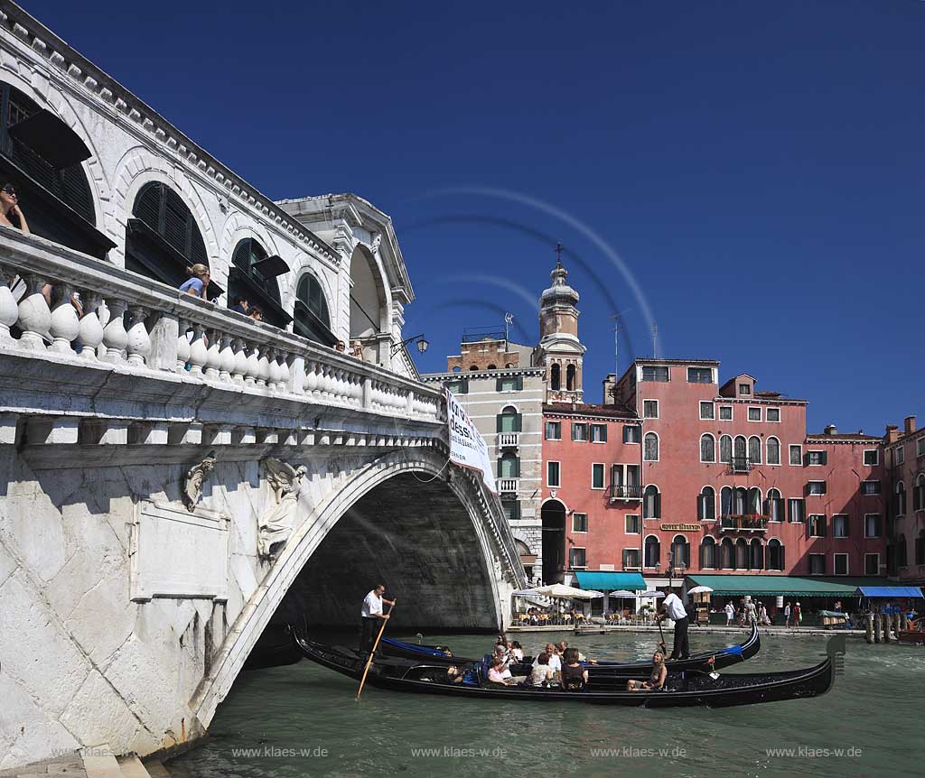 Venedig Bruecke Ponte di Rialto mit Kanal Grande seitlich fotografiert mit darunter herfahrender Gondel mit Gondoliere und jungem Paar, huebsche junge Frau in Gondel sitzend, Menschen auf Bruecke stehend, gegenueber Riva del Ferro mit dem Kirchturm Campanile der Kirche Chiesa di San Bartolomeo; Venice sideways view to bridge of Rialo with Canal Grande, a gondoa with gondolier and a young coule, a pretty young woman sitting inside of gondola in the background Riva del ferro with the tower of church of San Bartolomeo