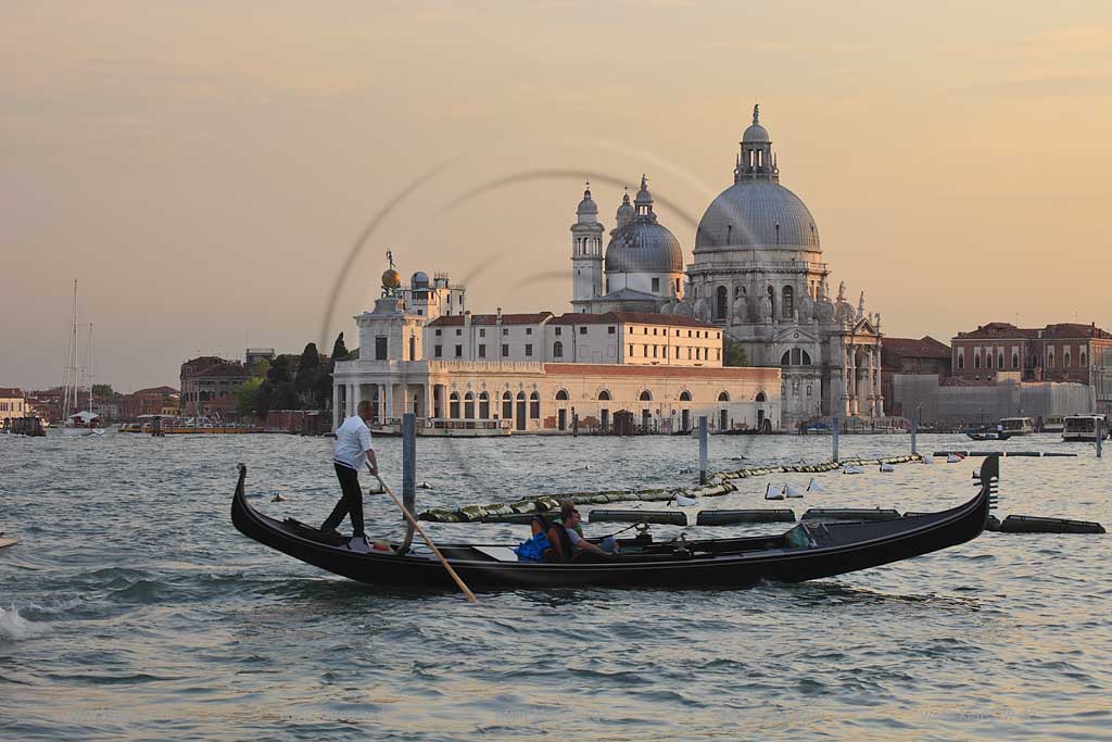 Venedig Blick von Riva degli Schiavoni ueber Kanal di San Marco mit Gondel, Gondoliere und jungem Paar in Gondel sitzend zur Basilika di Santa Maria della Salute im stimmungsvollen Licht der untergehenden Abensonne; Venice view from Riva degli Schiavoni with gondola, gondolier and young caple sitting in the gondola over canal di San Marco to basilica San Maria della Salute in romantoc sunset light