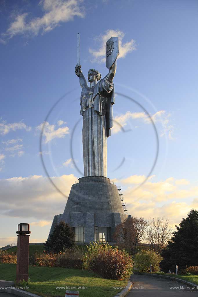 Kiew Statue der Mutter Heimat Rodina mat' mit Schwert und Schild im Park des Ruhmes  aus Metall 108 m hoch einschliesslich Sockel aufgenommen an einem klaren Herbsttag bei tiefstehendem Sonnenlicht stimmungsvoll blauer Himmel mit Wolken . National Museum about the History of the Great Patriotic War against Nazi-Germany with the large monument "Rodina Mat'", lit. 'Mother Home country'. The monument itself is more than 100 m high and reminds the visitor of the devastating but glorious fight against Hitler.