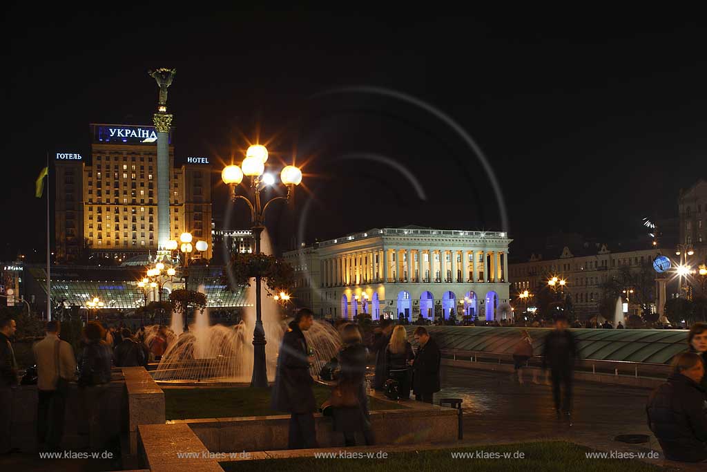 Kiew Springbrunnen vor der Saeule Sule des barocken 62 m hohen Monumentes der Unabhngigkeit mit goldenem Kapitell einer strengen Maedchenfigur Maid mit goldenem Zweig des Schneeballstrauches dahinter Hotel Ukraine Ukrajina rechts daneben das Opernstudio der Nationalen Musikakademie der Ukraine am Unabhaengigkeitsplatz Unabhngigkeitsplatz Majdan Nesaleshnosti  Majdan Nezaleznosti am Chrestschatyk Chrescatyk bei Nacht mit dem beleuchteten Globus mit dem in der Ukraine Entfernungen gemessen werden, Illumination, Wasserspielen und Menschen  . Maidan Nesaleshnosti - Independence Square at night The Khreschatyk rd. crosses Independece Square. This is Kiev's most expensive boulevard, where banks, office buildings, boutiques and chic restaurants line up.