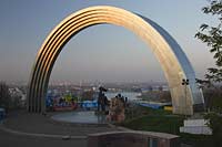 Kiew Blick vom Vladimirskaya Gorka Park durch den Bogen der Voelkerfreundschaft zwischen der Ukraine und Russland auf den Fluss Dnepr sowie die Hochhaeuser am Westufer im roetlichen Licht der untergehenden Sonne . The friendship Arch: sculptor A. Skoblikov and Architect I. Ivanov and others. Dedicated to the unification of Russia and Ukraine, but called "The Yoke" by kievans. The rainbow shape arch is 50 metres in diameter. Viewing deck were most of the east bank can be viewed, Troeschina and towards the north of city. Podil and Obolon. Undemeath the Friendship Arch are two statues. The left one is made from bronze and depicts a Russian and Ukrainian worker holding up the Soviet Order of Friendship of People the other one is made from granite and depicts the particants of the Pereyaslavska Rada of 1654.