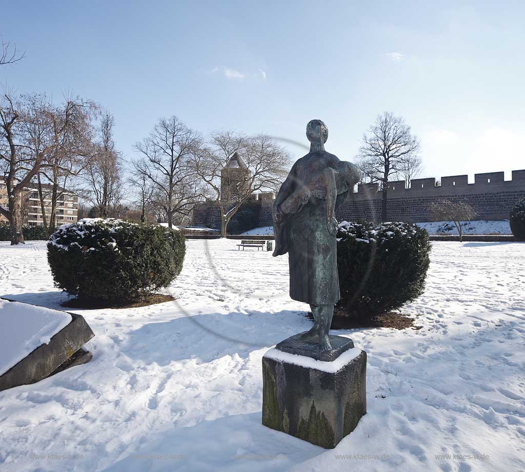 Koeln Altstadt, die Gereonsmhle ist Bestandteil eines etwa 300 m langen erhaltenen Restes der mittelalterlichen Stadtmauer von Koeln. Sie liegt zwischen Gereonswall und Hansaring westlich der Eigelsteintorburg, Ansicht im Winter mit Schnee. In dem kleinen Park am Hansaring (vor der Stadtmauer) erinnert die von dem niederlaendischen Bildhauer Mari Andriessen entworfene Bronzeskulptur Frau mit dem toten Kind an die nationalsozialistische Diktatur. Das Denkmal wurde 1959 enthuelllt. Es handelt sich um den zweiten Abguss eines Teils einer Figurengruppe, die zur Erinnerung an die Befreiung von der deutschen Besatzung in Enschede errichtet wurde; Cologne oldtown, histrical city wall with mill Gereonsmuehle in winter with bronze sculpture memorial in snow