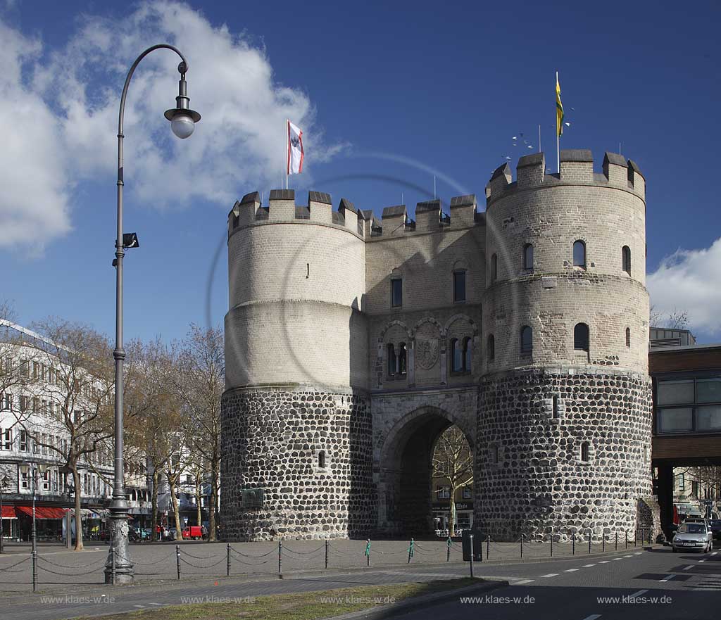 Koeln Altstadt Rudolfplatz mit Hahnentorburg Feldseite im Vorfruehling mit kahlen Baeumen, Kumuluswoilken und blauem Himmel, Cologne historical city gate in the old towm early spring time bare-brandched trees