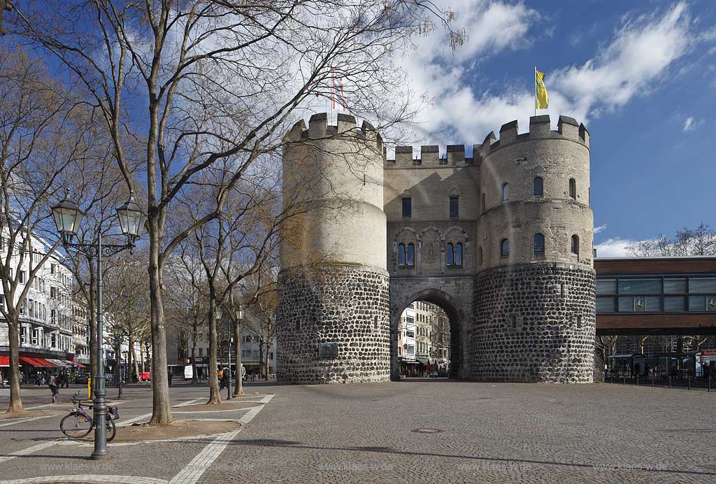 Koeln Altstadt Rudolfplatz mit Hahnentorburg Feldseite im Vorfruehling mit kahlen Baeumen, Kumuluswoilken und blauem Himmel, Cologne historical city gate in the old towm early spring time bare-brandched trees