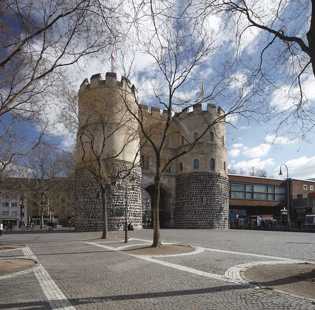 Koeln Altstadt Rudolfplatz mit Hahnentorburg Feldseite im Vorfruehling mit kahlen Baeumen, Kumuluswoilken und blauem Himmel, Cologne historical city gate in the old towm early spring time bare-brandched trees