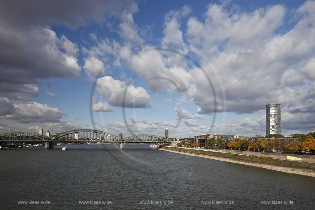 Koeln, Blick von der Deutzer Bruecke ueber den Rhein zur Hohenzollernbruecke mit Eisenbahn IC, dem Messeturm und Koelntriangel Hochhaus mit stimmungsvollem Wolkenhimmel; Cologne view from bridge Deutzer Bruecke to Hohenzollern bridge with IC rail, tower of fair and Colognetriangle with atmospheric clouds in the blue sky