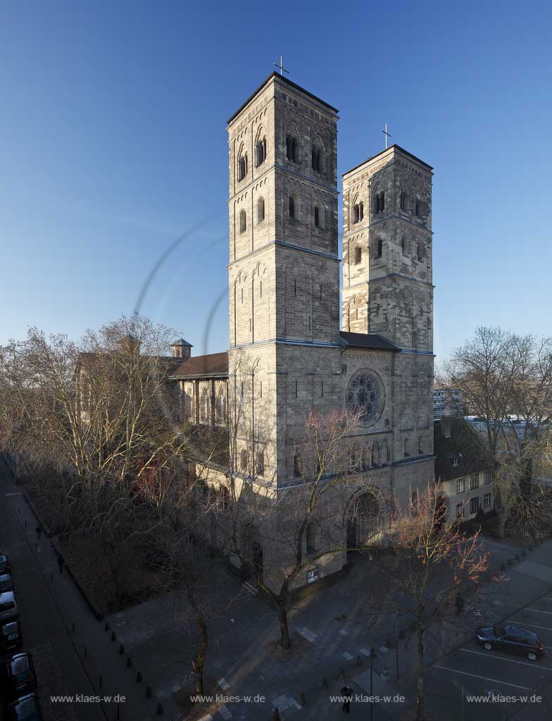 Koeln Deutz, Aussenansicht Hofseite von Nordosten zu den beiden Kirchtuermen der Pfeilerbasilika St. Heribert im Fruehling mit kahlen Baeumen im frueken Morgenlicht; Cologne Deutz northeast side with steeples of basilica St. Heribert