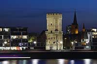 Koeln, der Bayenturm, mittelalterlicher Wehrturm, Sitz der Stiftung Frauenmediaturm in abendlicher Kunstlichtbeleuchtung, illuminiert, blaue Stunde, zwischen modernen Wohn- und Buerogebaeuden am Rheinauhafen, the Bayenturm, medieval defence tower in evening light, illlumination beween mordern buildings 