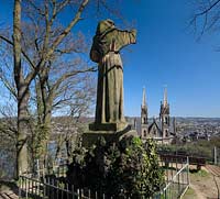 Remagen Apollinarisberg, die segnende Franziskustatue ist ein Symbol fr die Verbundenheit der Stadt Remagen mit dem Apollinarisberg und den Franziskanern, die rund 150 Jahre hier seelsorglich taetig waren. Im Jahr 1886 wurde die ueberlebensgross 3,8 meter hohe Statue auf den Anhoehe oberhalb der Apollinariskirche eingeweiht werden. Der Koelner Kuenstler Joseph Albermann hatte sie gestalte, Rueckseite, Rueckansicht von hinten mit Blick auf die Apollinariskirche im Fruehlungt Remagen sculture of Franziskus at the Apollinarisberg in springtime, rear side