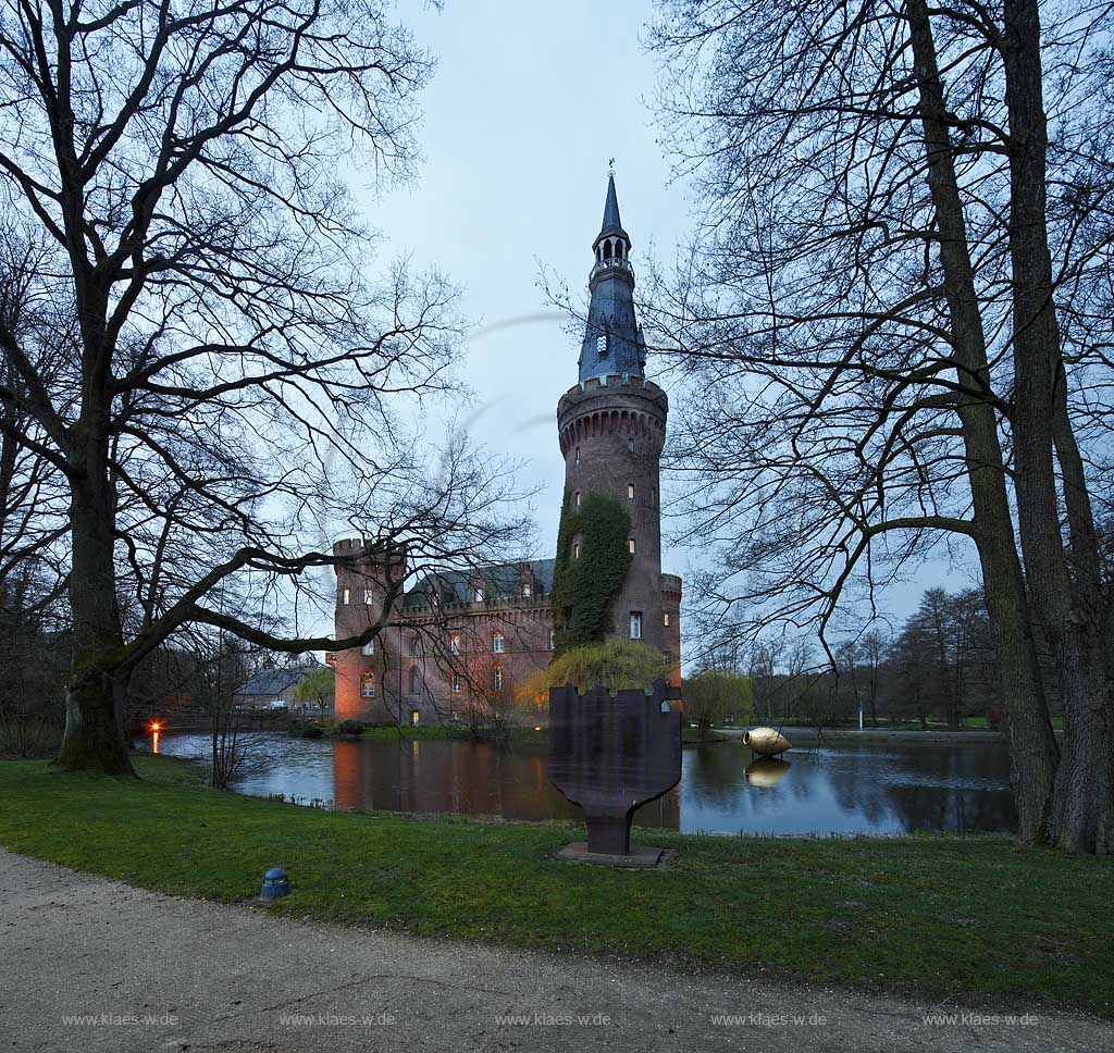Bedburg-Hau, Schloss Moyland im Fruehling mit kahlen Aesten zur blauen Stunde illuminiert, aktuelle Aufnahme mit dem neuen Helm auf dem Nordturm, Nordturmhelm; Bedburg-Hau castle Moyland in springtime during blue hour