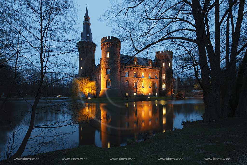 Bedburg-Hau, Schloss Moyland im Fruehling mit kahlen Aesten zur blauen Stunde illuminiert, aktuelle Aufnahme mit dem neuen Helm auf dem Nordturm, Nordturmhelm; Bedburg-Hau castle Moyland in springtime during blue hour