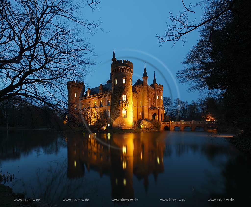 Bedburg-Hau, Schloss Moyland im Fruehling mit kahlen Aesten zur blauen Stunde illuminiert, aktuelle Aufnahme mit dem neuen Helm auf dem Nordturm, Nordturmhelm; Bedburg-Hau castle Moyland in springtime during blue hour