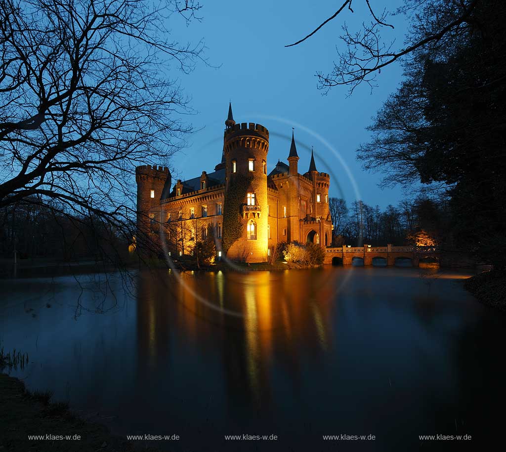 Bedburg-Hau, Schloss Moyland im Fruehling mit kahlen Aesten zur blauen Stunde illuminiert, aktuelle Aufnahme mit dem neuen Helm auf dem Nordturm, Nordturmhelm; Bedburg-Hau castle Moyland in springtime during blue hour