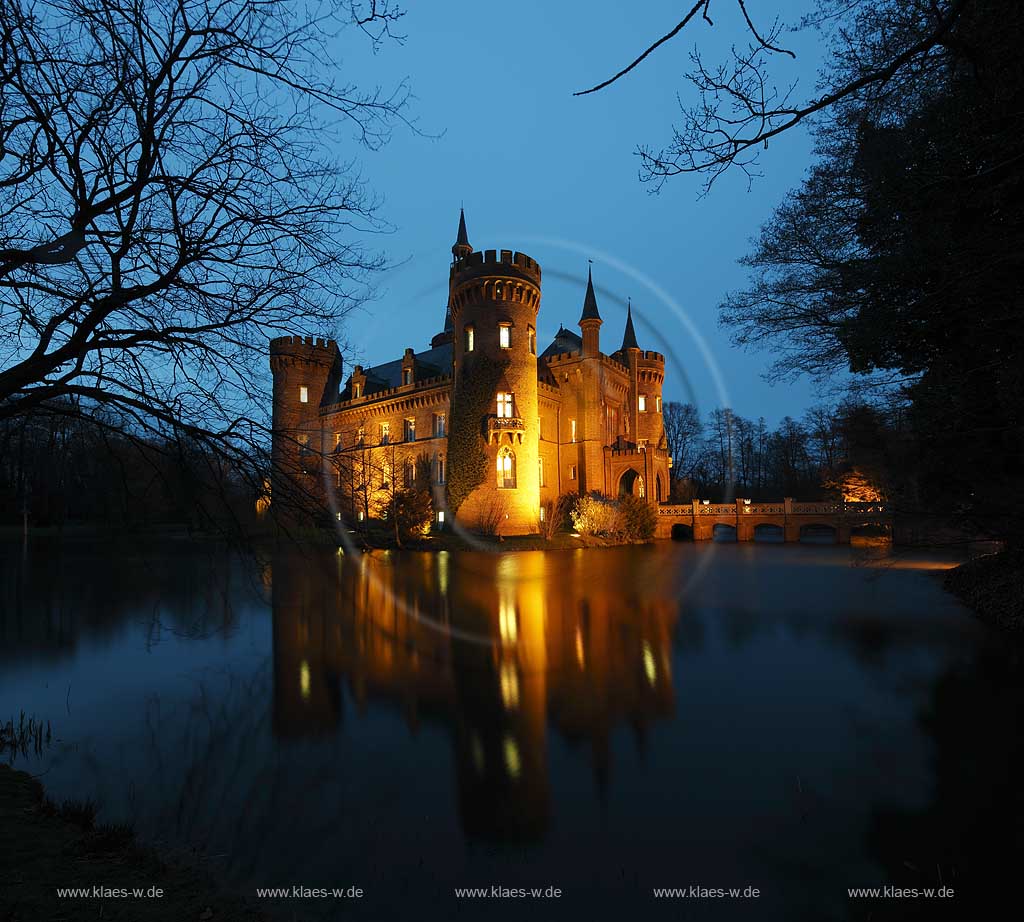 Bedburg-Hau, Schloss Moyland im Fruehling mit kahlen Aesten zur blauen Stunde illuminiert, aktuelle Aufnahme mit dem neuen Helm auf dem Nordturm, Nordturmhelm; Bedburg-Hau castle Moyland in springtime during blue hour