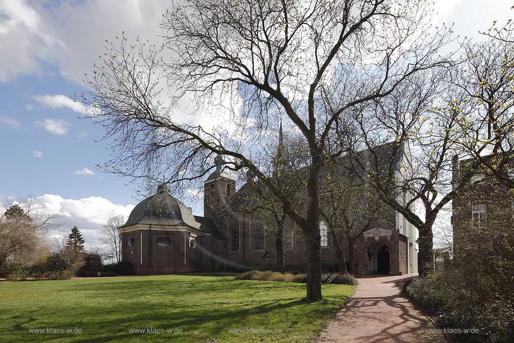 Kamp-Lintfort Abteiplatz mit Kloster Kamp im Fruehling mit kahlen Baeumen, Cumuluswolken, blauem Himmel im Fruehling, Gegenlicht, Kloster Kamp ist ein Kloster auf dem Gebiet der Stadt Kamp-Lintfort, deren Name sich vom Kloster herleitet. Es wurde 1123 gegruendet und war das erste Zisterzienserkloster im damaligen deutschsprachigen Raum. Die Klosteranlage liegt auf einem Huegel (Kamper Berg); Kamp-Lintfort abbey Kamp in spring with cumulus clouds and blue sky