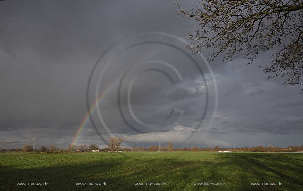 Kleve Niederrheinlandschaft mit Gehoeft mit Kollektoren, Solarenergie auf den Daechern,Strommasten und Stomleitungen,schwarzerHimmel, Sonnenschein und Regenbogen, kahle Baeume im Fruehling; Klever Netherrhine landscape with 