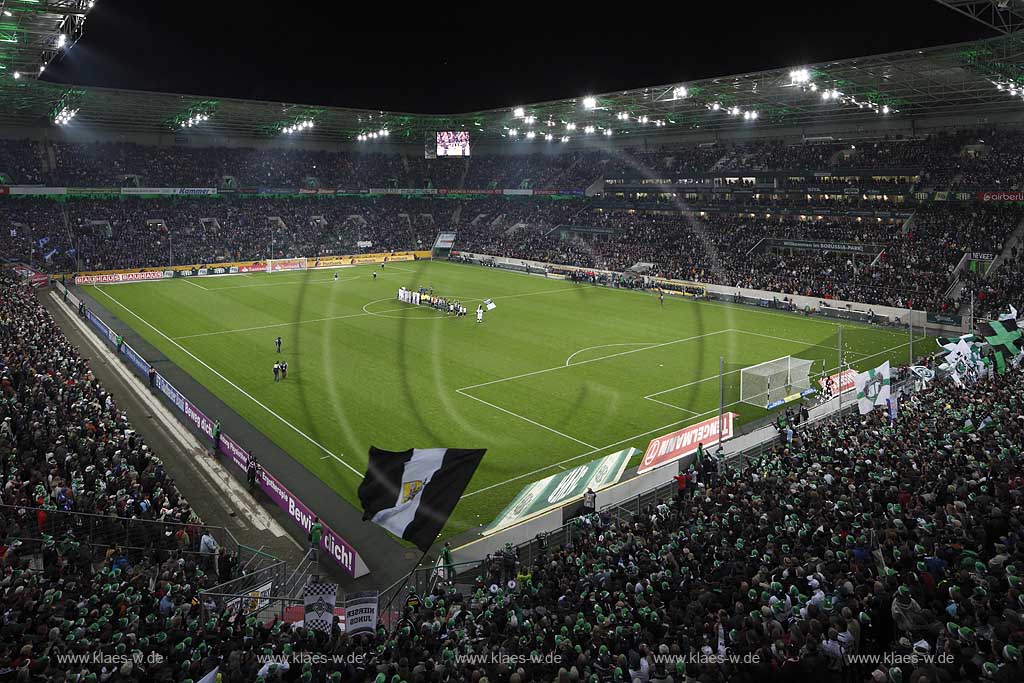 Moenchengladbach Borussiapark Stadion Innennansicht waehrend eines Fussballspiels Borussia Monchengladbach gegen FC Schalke 4 mit Flutlicht ausverkauft mit voll besetzten Raengen vor Spielbeginn; Mannschaften auf dem Spielfeld wehende Fahnren Fussballfans Zuschauer Tribuenen; Moenchengladbach Stadium internal picture during Football game Borussia Moenchengladbach vs. FC Schalke 04 with fans and flags