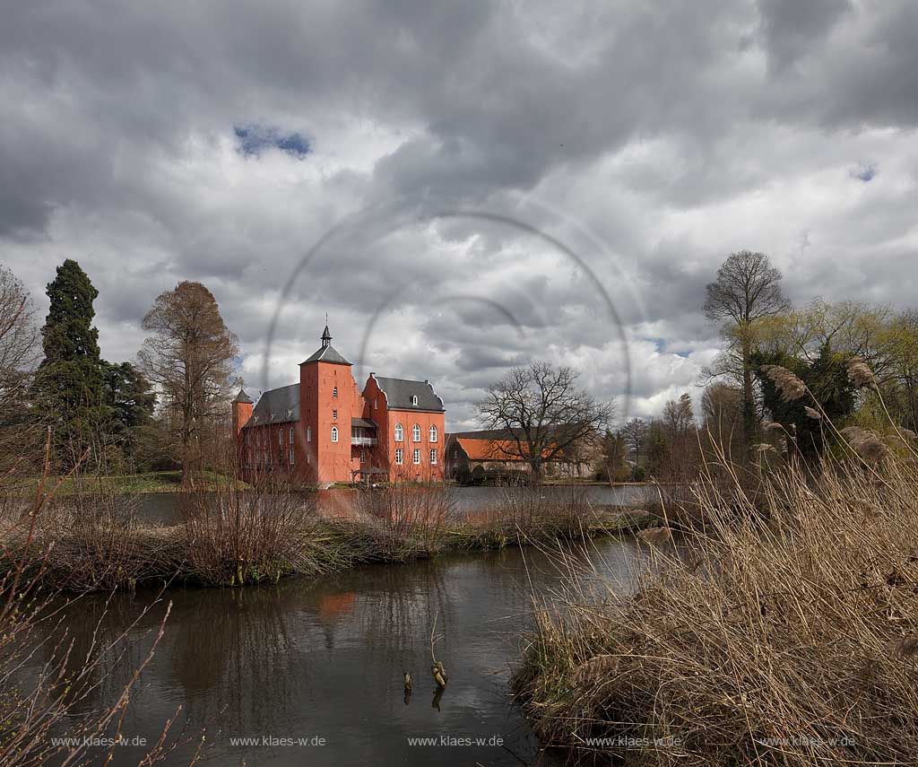 Neukirchen-Vlyn Schloss Bloemersheim, Wasserschloss aus dem Spaetmittelalter, Blick zur rueckwaertigen Seite ueber den Schlossweiher im Fruehling mit kahlen Bauemen,Wolkenstimmung windig bis stuermisch; Kamp-Lintfort water moated castle Bloemersheim in springtime  impression with clouds