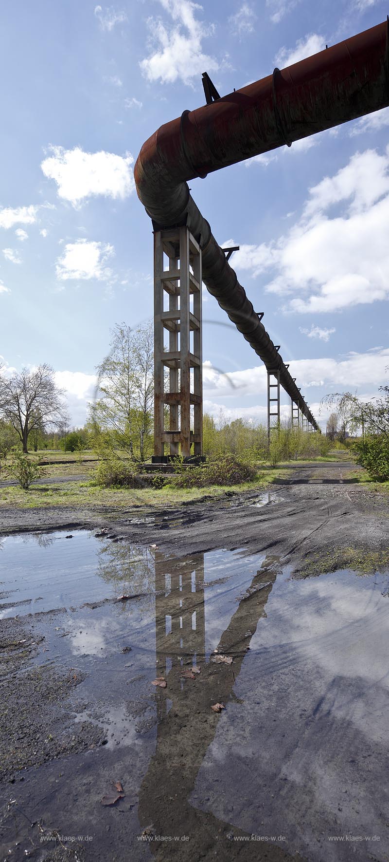 Duisburg Meiderich. Nacktflaeche auf dem Zechengelaende mit Hochgasleitung und Spiegelbild in Wasserlache auf Schlackegrund. Der Landschaftspark Duisburg-Nord, auch kurz LaPaDu ist ein etwa 200 Hektar groer Landschaftspark rund um ein stillgelegtes Huettenwerk in Duisburg-Meiderich, das im Rahmen der IBA (Internationale Bauausstellung Emscher Park) entstand. Der Landschaftspark ist einer der Ankerpunkte der Europaeischen Route der Industriekultur sowie der Route der Industriekultur im Ruhrgebiet;  Duisburg-Meiderich, the Meiderich ironworks are the main feature in the North Duisburg Landscape Park, naked aere at cole mine aera with hight gas line.