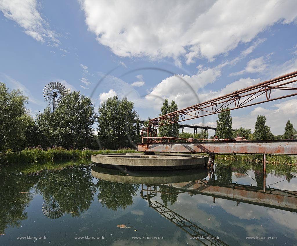 Duisburg Meiderich. Rundklaerbecken, Bock-Kran, Blut-Weiderich und Windrad im Hintergrund, Wolkenstimmung. Der Landschaftspark Duisburg-Nord, auch kurz LaPaDu ist ein etwa 200 Hektar grosser Landschaftspark rund um ein stillgelegtes Huettenwerk in Duisburg-Meiderich, das im Rahmen der IBA (Internationale Bauausstellung Emscher Park) entstand. Der Landschaftspark ist einer der Ankerpunkte der Europaeischen Route der Industriekultur sowie der Route der Industriekultur im Ruhrgebiet;  Duisburg-Meiderich, the Meiderich ironworks are the main feature in the North Duisburg Landscape Park, sedimentation tank