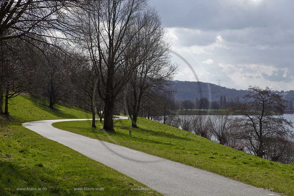 Kemnader See, Landschaft mit Weg, geschwungen, einsam in Fruehlingslandschaft mit kahlen Baeumen im Gegenlicht; Landscape with a path at lake Kemnade in springtime, bare-branched trees, cumulus clouds