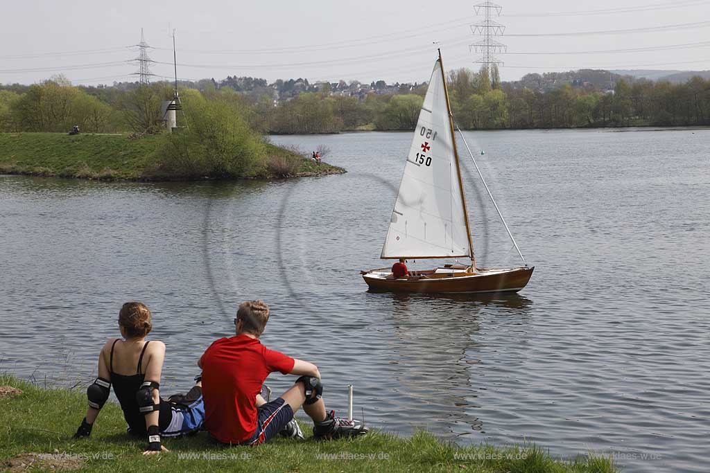 Kemnader see, rastende Inliner, Inline scater am Seeufer sitzend und in Richung See blickend mit fahrendem Segelboot auf dem Wasser, Inlinse scater which take a break, stting at the waerside of lake Kemnade with sailboat sailing on the water