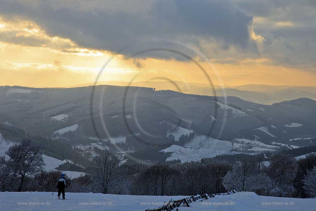 Sundern Wildewiese, Blick vom Schomberg im Skigebiet in Abenstimmung, Wolkenstimmung und Fernblick ins Sauerland, Skilift und Skifahrer im Gegenlicht, Sonnenuntergang; Skiing region Wildewiese with ski tourists and ski lift in impressive sunset light and dark clouds