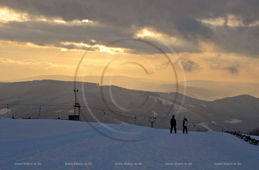 Sundern Wildewiese, Blick vom Schomberg im Skigebiet in Abenstimmung, Wolkenstimmung und Fernblick ins Sauerland, Skilift und Skifahrer im Gegenlicht, Sonnenuntergang; Skiing region Wildewiese with ski tourists and ski lift in impressive sunset light and dark clouds