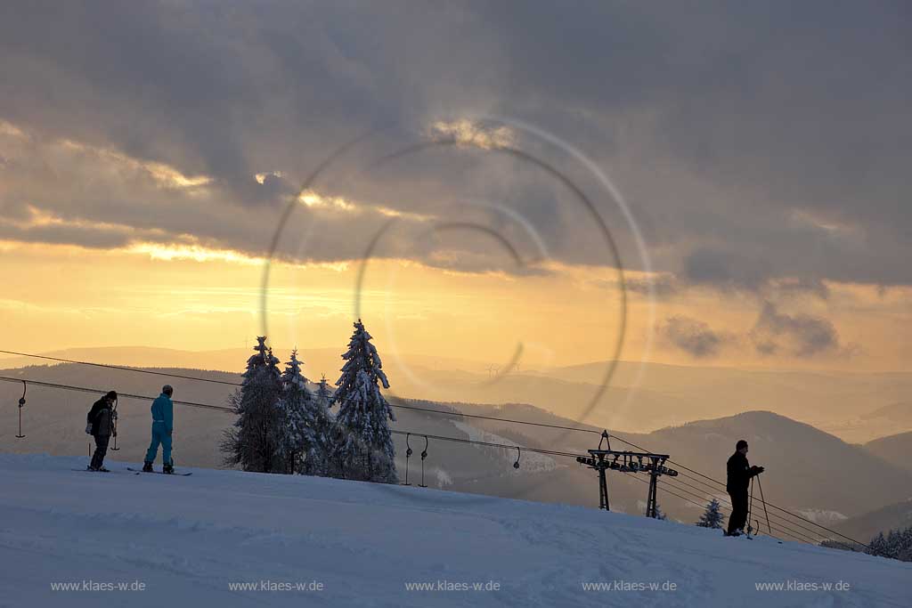 Sundern Wildewiese, Blick vom Schomberg im Skigebiet in Abenstimmung, Wolkenstimmung und Fernblick ins Sauerland, Skilift und Skifahrer im Gegenlicht, Sonnenuntergang; Skiing region Wildewiese with ski tourists and ski lift in impressive sunset light and dark clouds