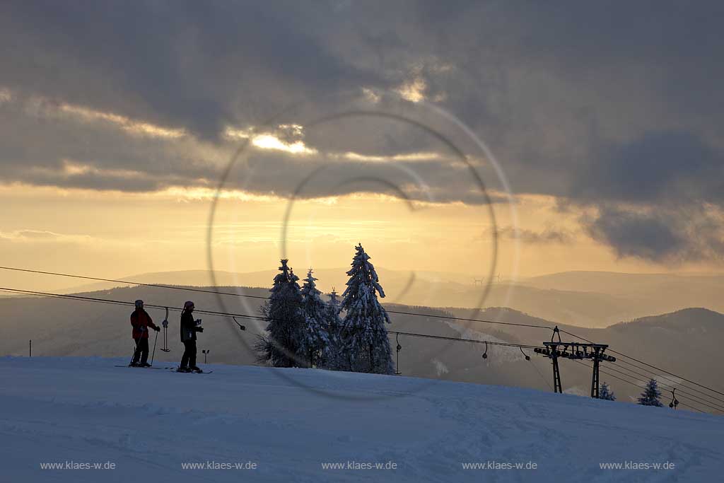 Sundern Wildewiese, Blick vom Schomberg im Skigebiet in Abenstimmung, Wolkenstimmung und Fernblick ins Sauerland, Skilift und Skifahrer im Gegenlicht, Sonnenuntergang; Skiing region Wildewiese with ski tourists and ski lift in impressive sunset light and dark clouds