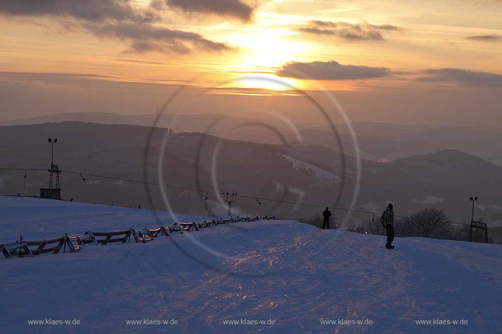 Sundern Wildewiese, Blick vom Schomberg im Skigebiet in Abenstimmung, Wolkenstimmung und Fernblick ins Sauerland, Skilift und Skifahrer im Gegenlicht, Sonnenuntergang; Skiing region Wildewiese with ski tourists and ski lift in impressive sunset light and dark clouds