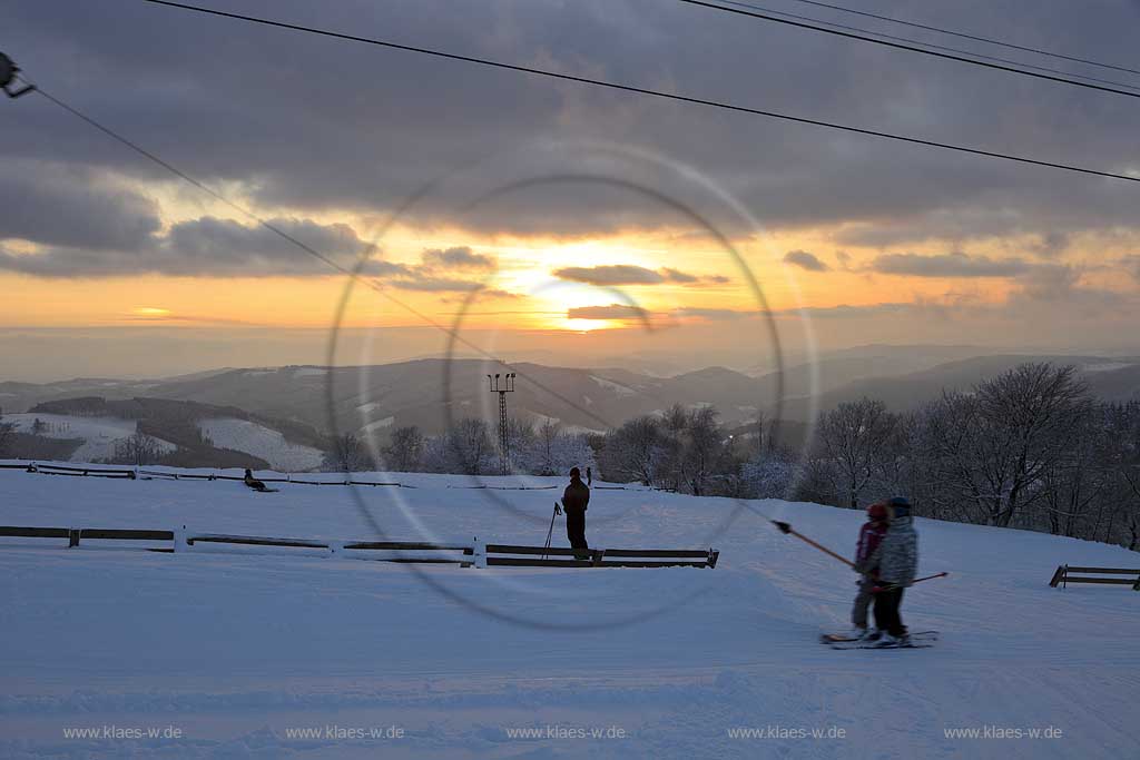 Sundern Wildewiese, Blick vom Schomberg im Skigebiet in Abenstimmung, Wolkenstimmung und Fernblick ins Sauerland, Skilift und Skifahrer im Gegenlicht, Sonnenuntergang; Skiing region Wildewiese with ski tourists and ski lift in impressive sunset light and dark clouds