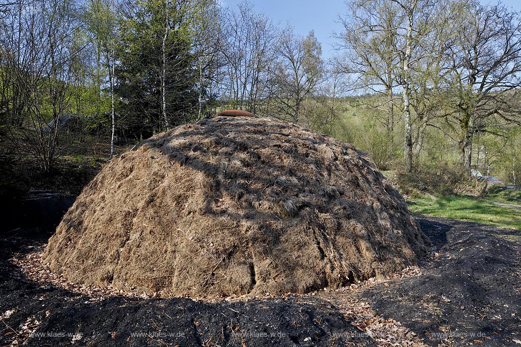 Netphen Walpersdorf, Kohlenmeiler Walpersdorf, einziger noch betriebener Kohlenmeiler im Siegerland. Die Koehlerei zur Herstellung von Holzkohle hat im Siegerland auf Grund der Eisenverhuettung eine lange Tradition; Netphan Walpersdorf traditional charcoal kiln in springtime landscape